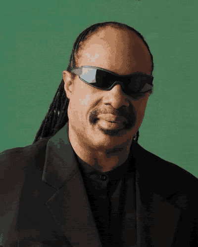a close up of a man wearing sunglasses and a suit against a green background