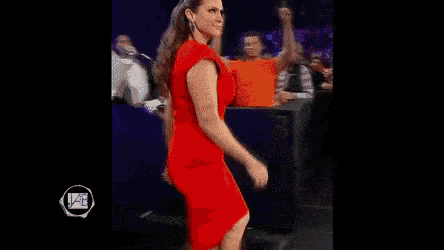 a woman in a red dress is walking on a stage in front of a crowd of people .