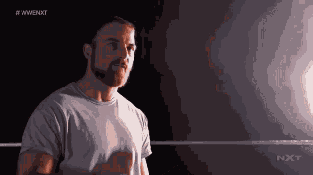 a man with a beard is standing in a wrestling ring with the letters nxt on the bottom right