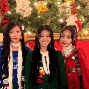 a group of three girls are posing for a picture in front of a christmas tree .