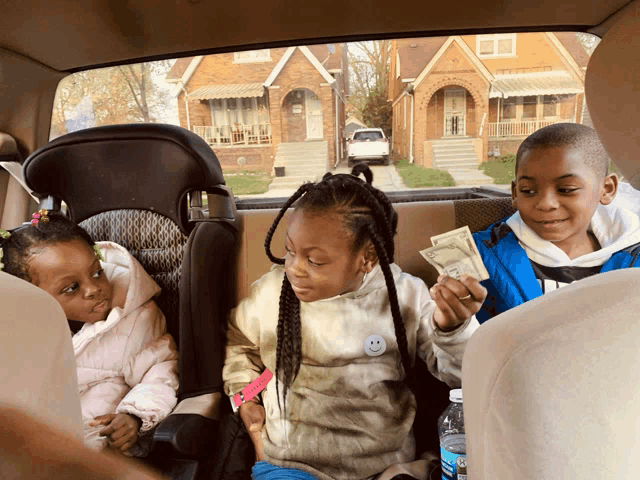 a boy and two girls are sitting in the back seat of a car holding money