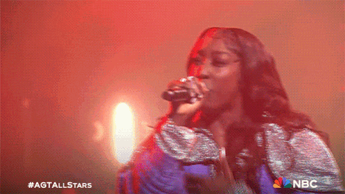 a woman singing into a microphone with a nbc logo in the corner