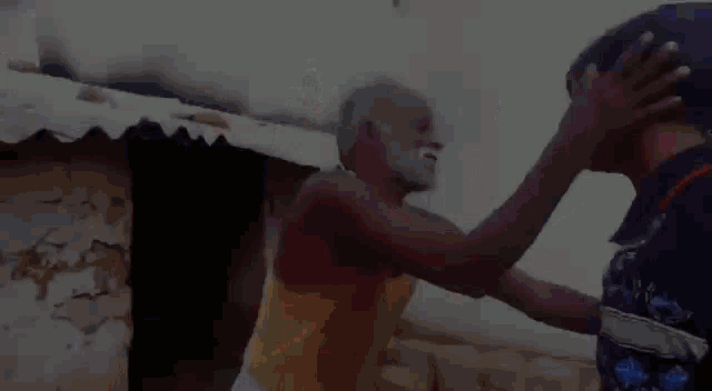 a man is holding another man 's head while standing in front of a hut .