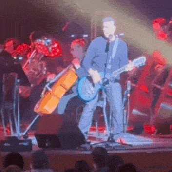 a man singing into a microphone while playing a guitar on stage