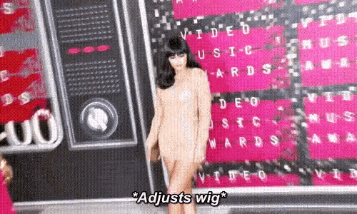 a woman wearing a wig is standing on a red carpet at awards .