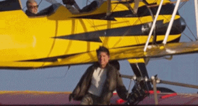 a man is sitting on the ground in front of a yellow and black airplane