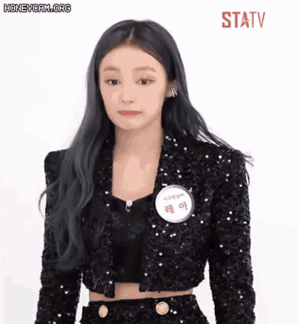a woman wearing a black sequined jacket with a name tag on her chest .