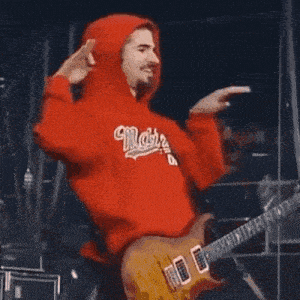 a man wearing a red hoodie is playing a guitar .