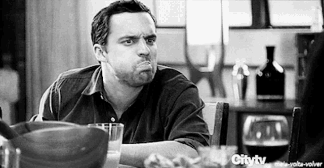 a man is sitting at a table with a glass of wine making a funny face .