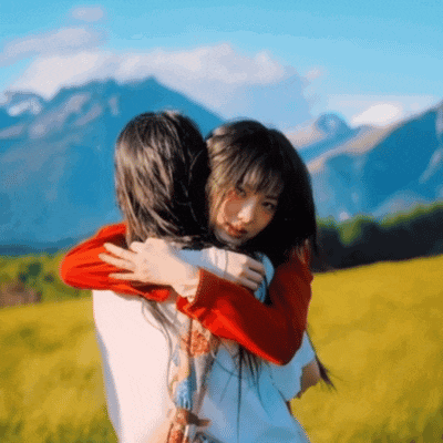 two girls are hugging each other in a field with mountains in the background