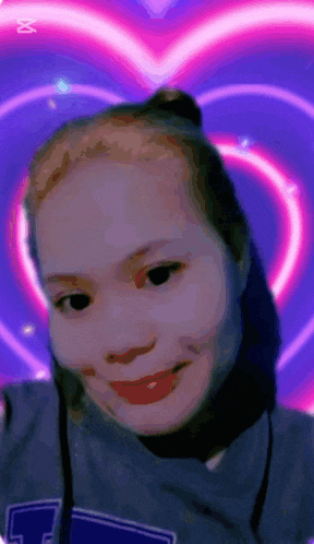 a woman in a blue shirt with the letter t on it smiles in front of a pink heart