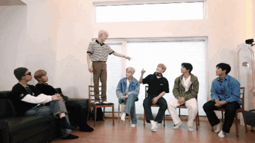 a group of young men are sitting in chairs and a man is standing on a couch