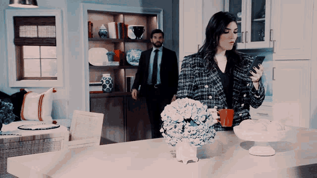 a man in a suit stands behind a woman looking at her cell phone