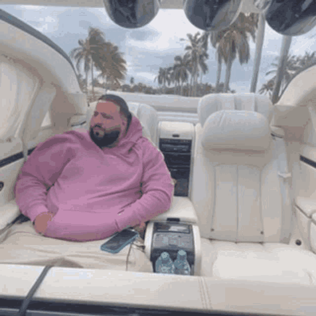 a man in a pink sweatshirt is sitting in the back seat of a car .