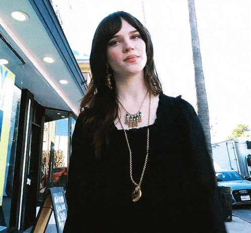 a woman wearing a black top and a gold necklace stands in front of a sign that says " ice cream "