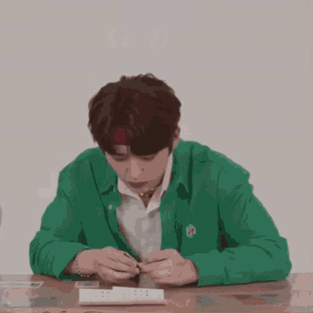 a young man wearing a green jacket and a red headband is sitting at a table playing cards .