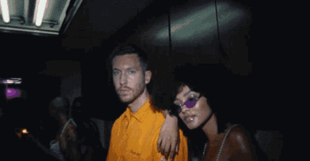 a man in an orange shirt is standing next to a woman wearing purple sunglasses
