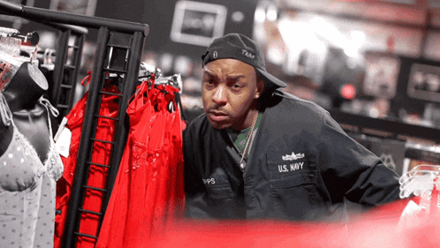 a man in a u.s. navy uniform looks at red shirts on a rack