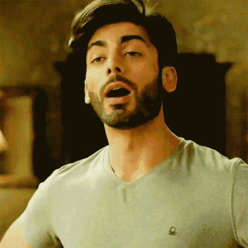 a man with a beard is wearing a benetton t-shirt and making a funny face .