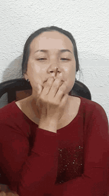 a woman covering her mouth with her hands while wearing a red shirt