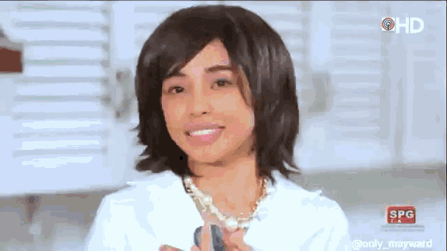 a woman wearing a wig and a pearl necklace is smiling in front of a sign that says spg on it