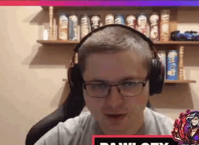 a man wearing headphones and glasses is sitting in front of a shelf full of chips .