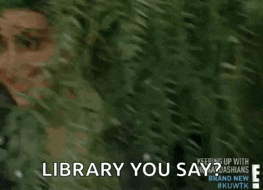 a woman is peeking out from behind a bush and smiling while talking to someone .