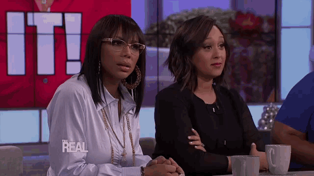 two women are sitting at a table in front of a sign that says it on it