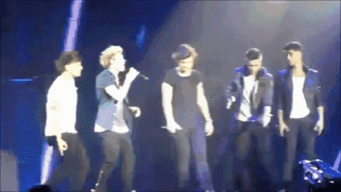 a group of men are standing on a stage and one of them is singing into a microphone .