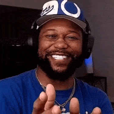 a man wearing headphones and a blue shirt is smiling and making a peace sign .
