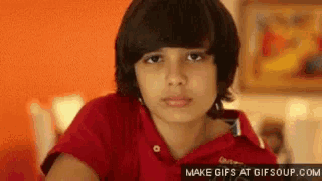 a young boy in a red shirt is looking at the camera and making a funny face .
