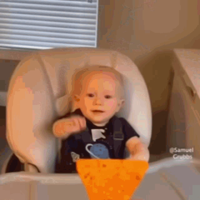 a baby sitting in a high chair with a piece of cheese in front of him .