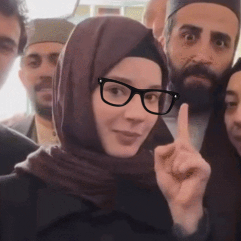 a woman wearing glasses and a hijab points her finger