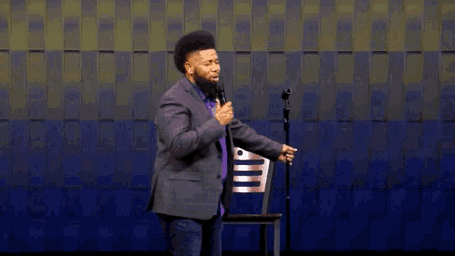 a man in a purple suit is standing in front of a microphone in front of a chair .
