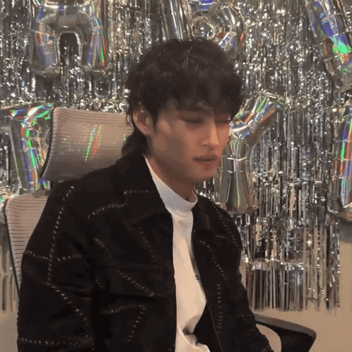 a man in a black jacket is sitting in a chair in front of balloons with the letter h on them