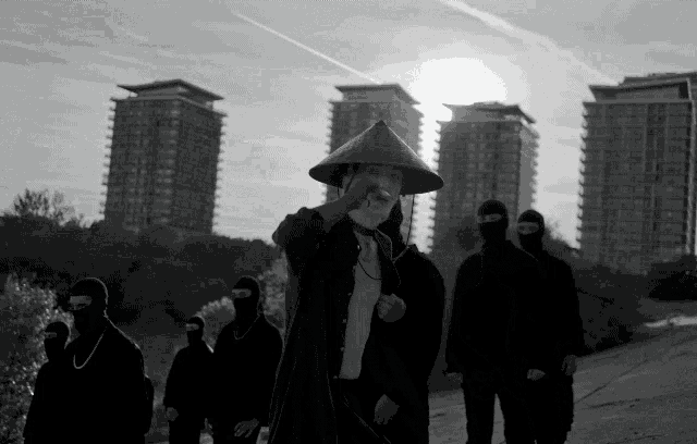 a man in a conical hat stands in front of a group of masked people