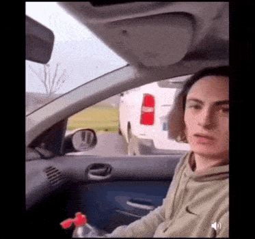 a young man is sitting in the driver 's seat of a car holding a bottle .
