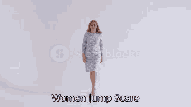 a woman is standing in front of a white wall and smiling while saying `` women jump scare '' .