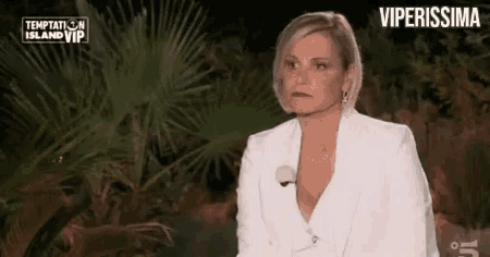 a woman in a white suit is sitting in front of a palm tree in a dark room .