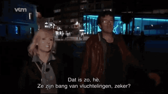 a man and a woman are standing in front of a vtm building