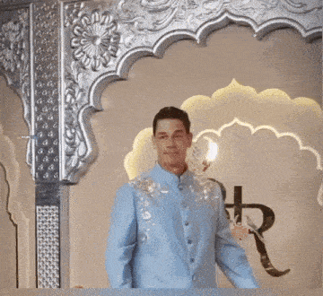 a man in a light blue suit stands in front of a silver archway