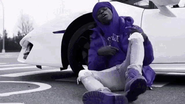 a man in a purple jacket is sitting in front of a white car .