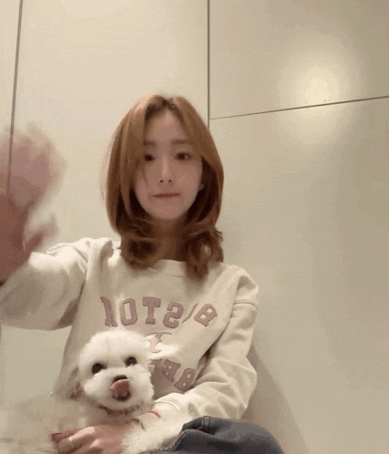 a woman wearing a sweatshirt that says 10t2 / 8 holds a white dog