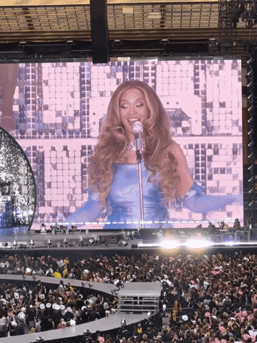 a woman in a blue dress is singing into a microphone in front of a large screen that says ' beyonce ' on it