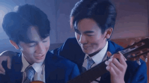 two men in suits and ties are holding a guitar and kissing each other .