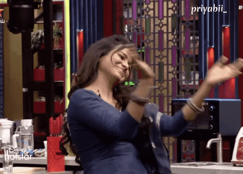 a woman is dancing in a kitchen with a disney hotstar logo behind her