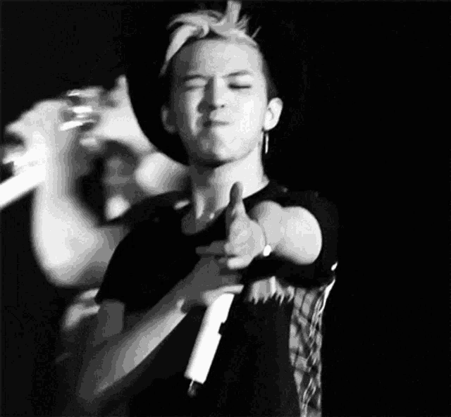 a black and white photo of a man holding a microphone and giving a thumbs up sign .