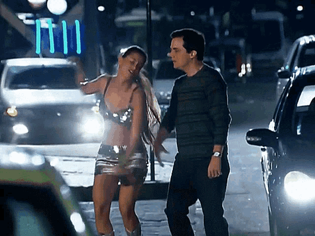 a man and a woman are walking down a street with cars behind them