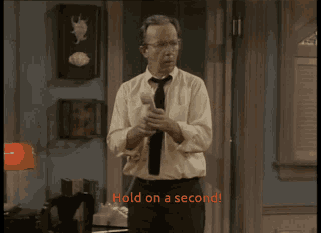 a man in a white shirt and tie is holding a hammer and says hold on a second