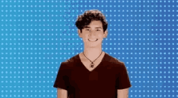a young man wearing a necklace with the letter n on it smiles in front of a blue background